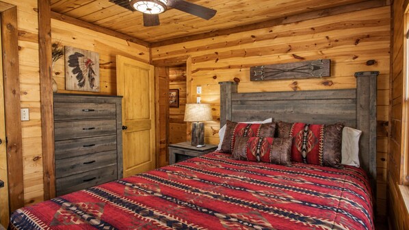A wooden cabin bedroom with a bed, dresser, and a ceiling fan.