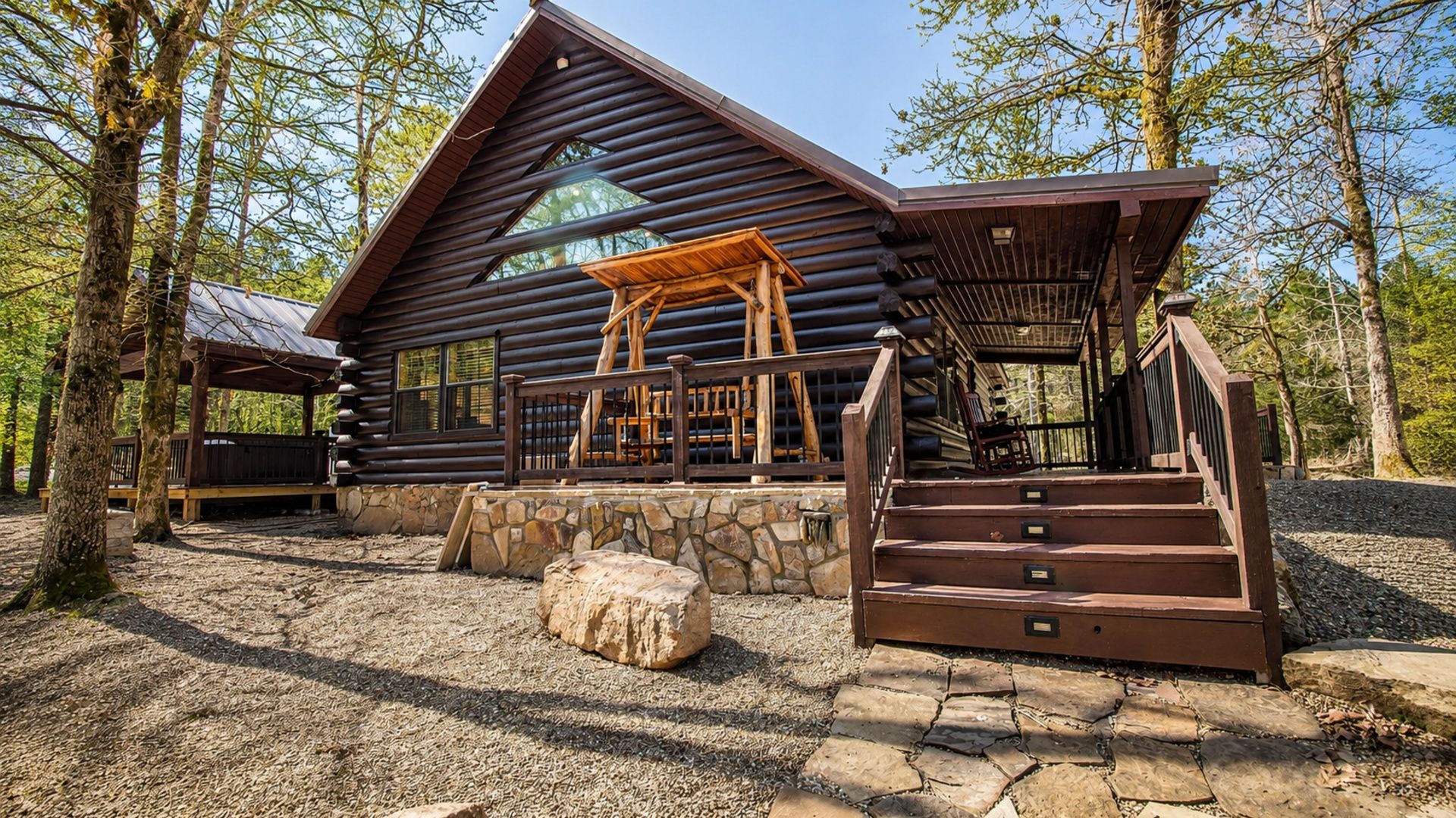 A log cabin with a stone foundation, wooden porch, and a staircase leading to the entrance.