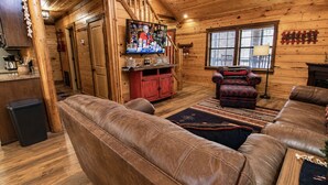 Een knus houten interieur met een televisie aan de muur, een rode kast en een leren bank.