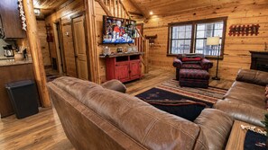 Een knus houten interieur met een televisie aan de muur, een rode kast en een leren bank.