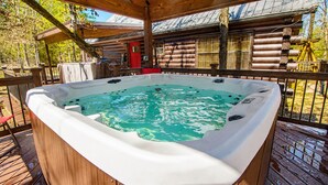 Un bain à remous sur une terrasse en bois, avec une cabane en rondins en arrière-plan.