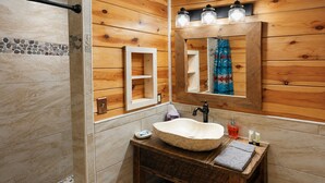 Une salle de bain avec un lavabo en pierre, des murs en bois, un miroir et un espace douche.