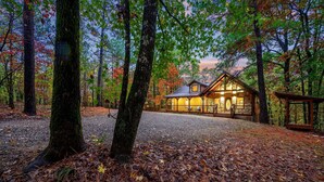 A cabin in a forest with a gravel driveway and a wooden deck. - Logan's Bluff Cabin at Hochatown (Broken Bow)