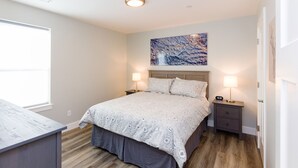 A bedroom with a bed, two bedside tables, a nightstand, a window, and a wall-mounted artwork.