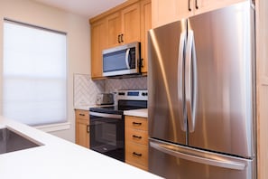 Une cuisine moderne dotée d’appareils électroménagers en acier inoxydable, de meubles de rangement en bois et d’un four à micro-ondes placé au-dessus de la cuisinière.