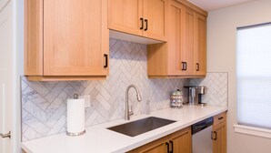 A modern kitchen with wooden cabinets, a white countertop, a stainless steel sink, and a coffee maker.