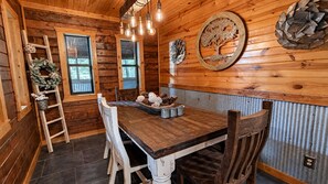 Ein Holzinterieur mit einem Esstisch, Stühlen, einer Chandelieber und Wanddekoration.