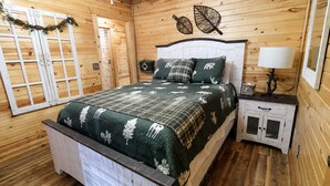 Een slaapkamer in een houten hutje, met een bed, nachtkastje en een wandlamp.