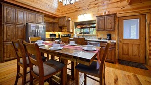 A wooden cabin-style kitchen with a dining table set for four, wooden cabinets, and a large window.
