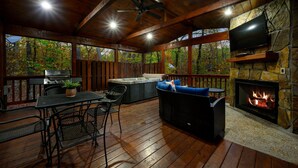 A covered outdoor area with a stone fireplace, a hot tub, and a grill.