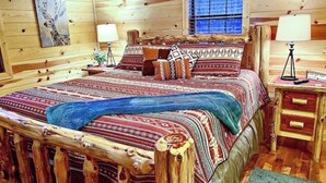 A wooden cabin bedroom with a bed, pillows, a nightstand, and a window.