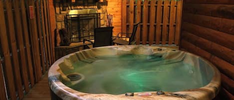 Ein Whirlpool mit Steinfassade, umgeben von Holzwänden und einem Steinkamin.