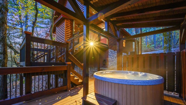 A wooden deck with a hot tub, wooden stairs, and a stone wall.