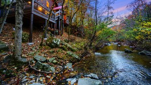 A traditional wooden building with a balcony overlooking a stream, surrounded by autumn foliage.