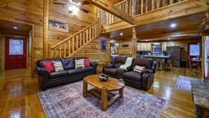 A spacious living area with a wooden ceiling, a central coffee table, two leather sofas, and a kitchen in the background.