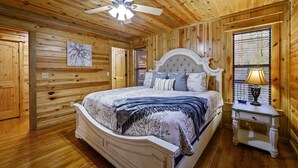 A wooden-paneled bedroom with a bed, a nightstand, a lamp, and a ceiling fan.