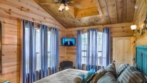 Camera da letto in una baita di legno, con un letto, tende, una televisione e una ventola a soffitto.
