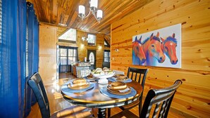 Un interior de madera con una mesa de comedor preparada para cuatro, un cuadro de caballos en la pared y una cocina al fondo.