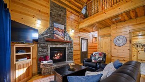 Interior acogedor de una cabaña de troncos con chimenea de piedra, sofá de cuero y un reloj colgado.