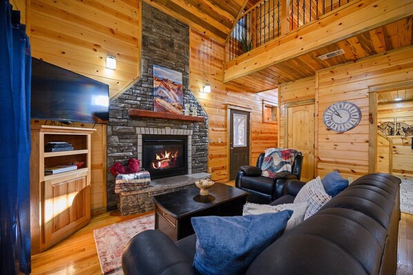 A cozy log cabin interior with a stone fireplace, leather sofa, and a mounted clock.