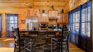Una cocina rústica con armarios de madera, una isla de piedra y una zona de bar con taburetes.