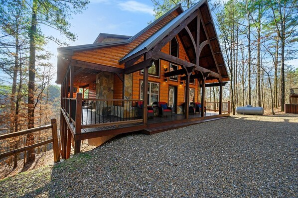 A log cabin with a porch, stone walls, and a gravel driveway.