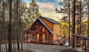 A log cabin with a porch, surrounded by trees.