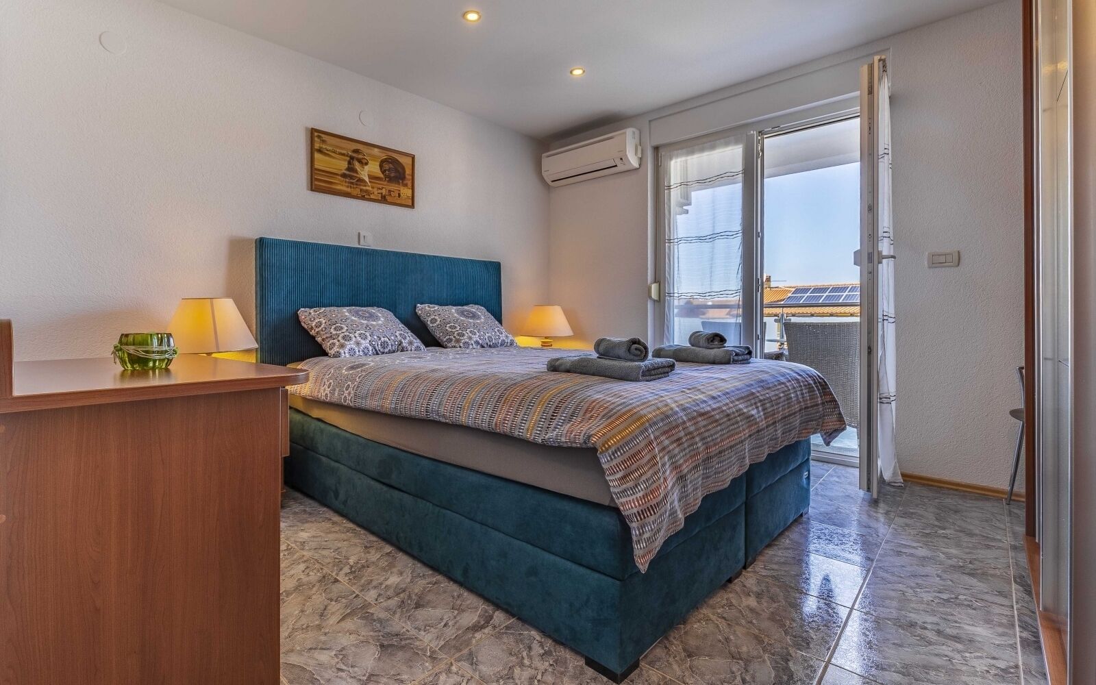 Quarto com cama, escrivaninha, cadeira, janela e ar condicionado.