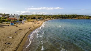 A beach with clear waters, a sandy shore, and buildings in the background. - Theos village apartments (Chania)