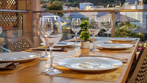 A dining table set with plates, glasses, and a small plant, overlooking a cityscape. - Theos village apartments (Chania)