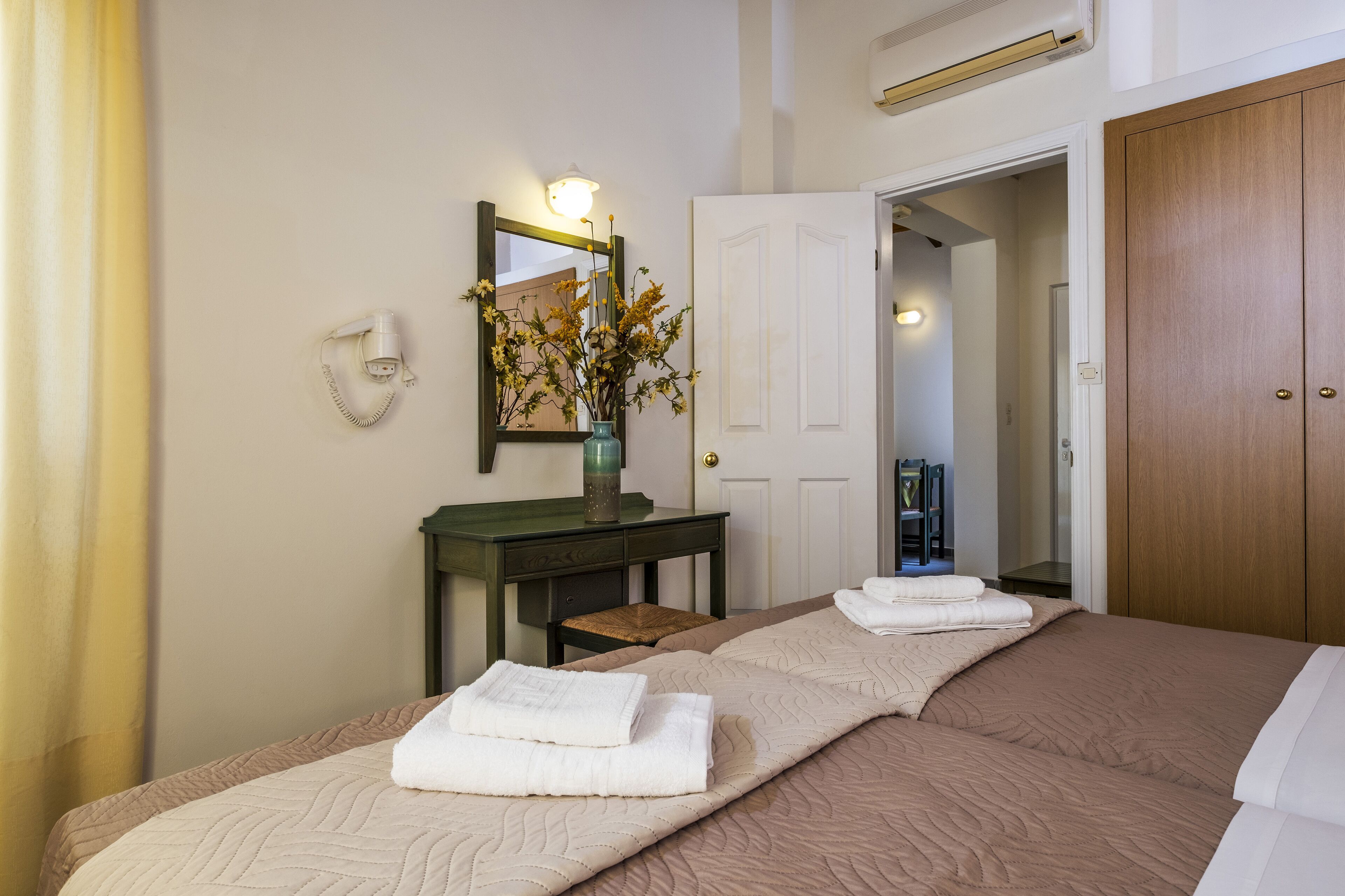 A hotel room with a bed, a desk, a mirror, and a door.