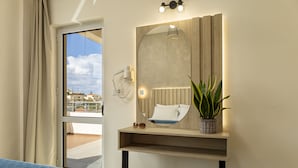 A hotel room with a bed, a bedside table with a plant, a mirror, and a window with curtains. - Theos village apartments (Chania)