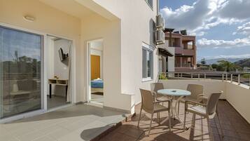 A balcony with a table and chairs, a sliding glass door, and a view of a building with air conditioning units.
