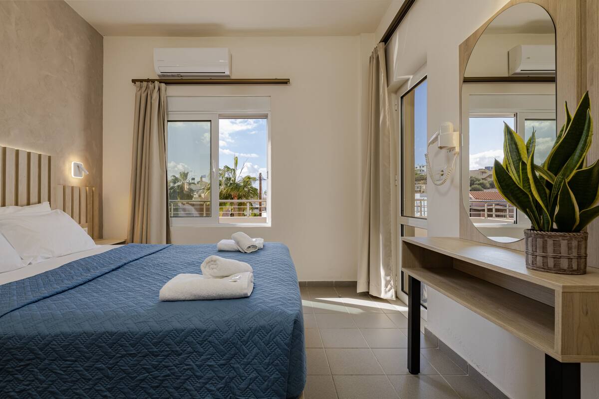 A hotel room with a bed, a bedside table, a mirror, and a window with curtains.