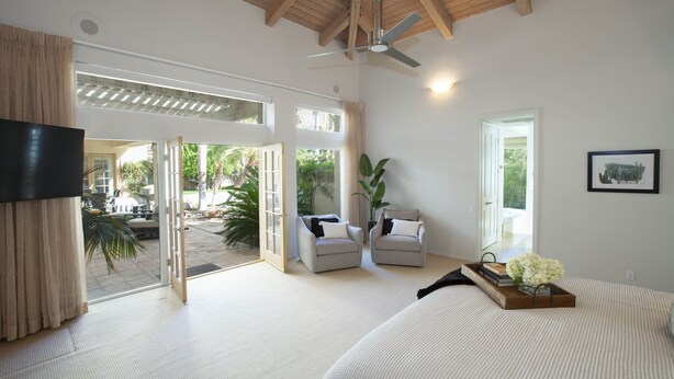A spacious bedroom with a large bed, two armchairs, a ceiling fan, and a sliding glass door leading to an outdoor area. - 30 Days+ at a Palm Springs Oasis (Palm Springs)