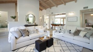 A spacious living room with two white sofas, a coffee table, and a billiards table in the background. - 30 Days+ at a Palm Springs Oasis (Palm Springs)