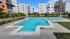 Zona de piscina con dos piscinas, rodeada por una valla y junto a edificios residenciales.