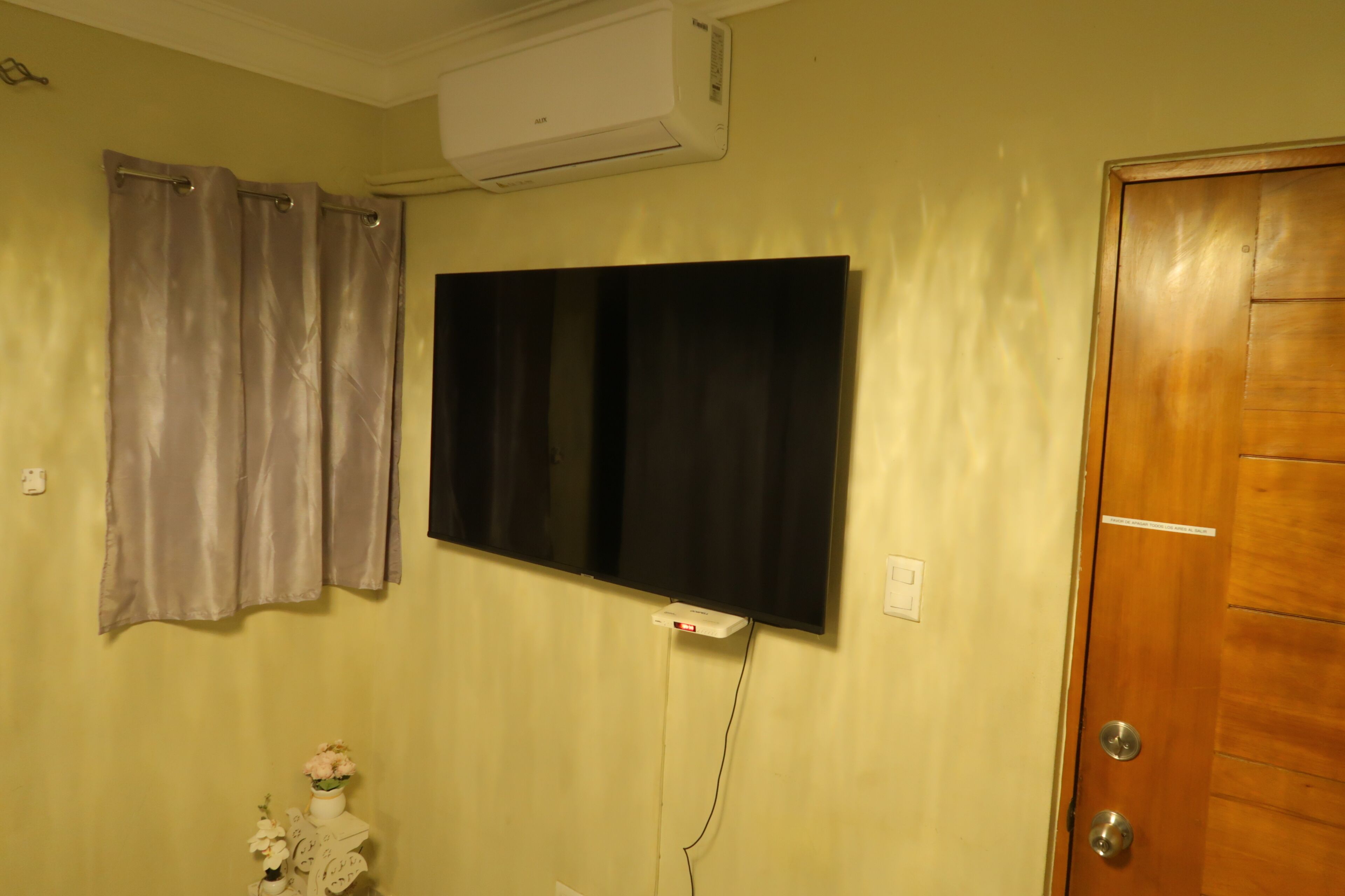 A bathroom with a shower curtain, a mounted television, and a wooden door.