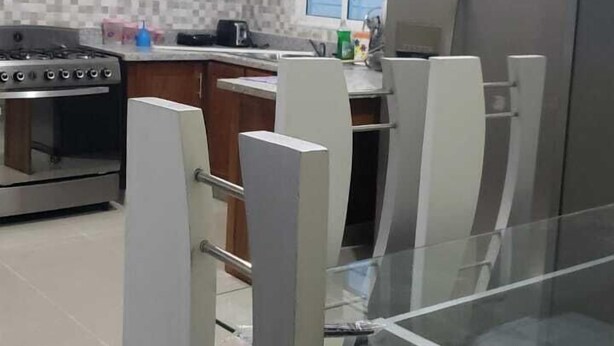 Una cocina moderna con armarios de madera, estufa a gas, refrigerador y mesa de vidrio con sillas.