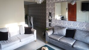 Un salón con dos sofás grises, una araña, un espejo y un cartel que dice 'HOME'.