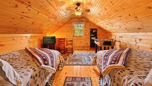 A cozy attic bedroom with wooden walls and a sloped ceiling. There are two beds with patterned bedding, a small desk, and a chair. A window provides natural light. - Stunning Mountain Views!!! Secluded Log Cabin with Hot Tub near West Jefferson  (Lansing)