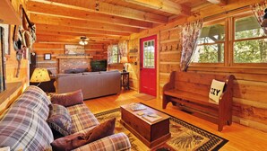 A cozy cabin interior with a wooden ceiling, a red door, a sofa, a bench, and a fireplace. - Stunning Mountain Views!!! Secluded Log Cabin with Hot Tub near West Jefferson  (Lansing)