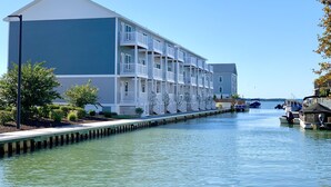 A multi-story hotel with balconies, located next to a body of water with boats. - IslandCoveParadise: Luxury-NewlyBuiltTH! OnTheWater-Boardwalk-Pool-w/2 CarGarage (Ocean City)