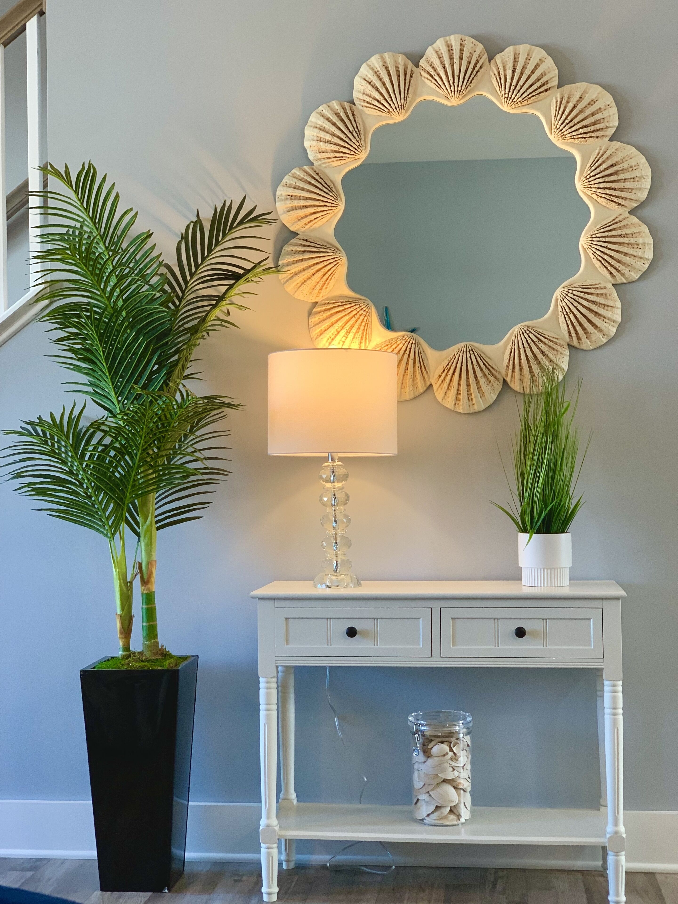 A white console table with a mirror, a lamp, and a potted plant.