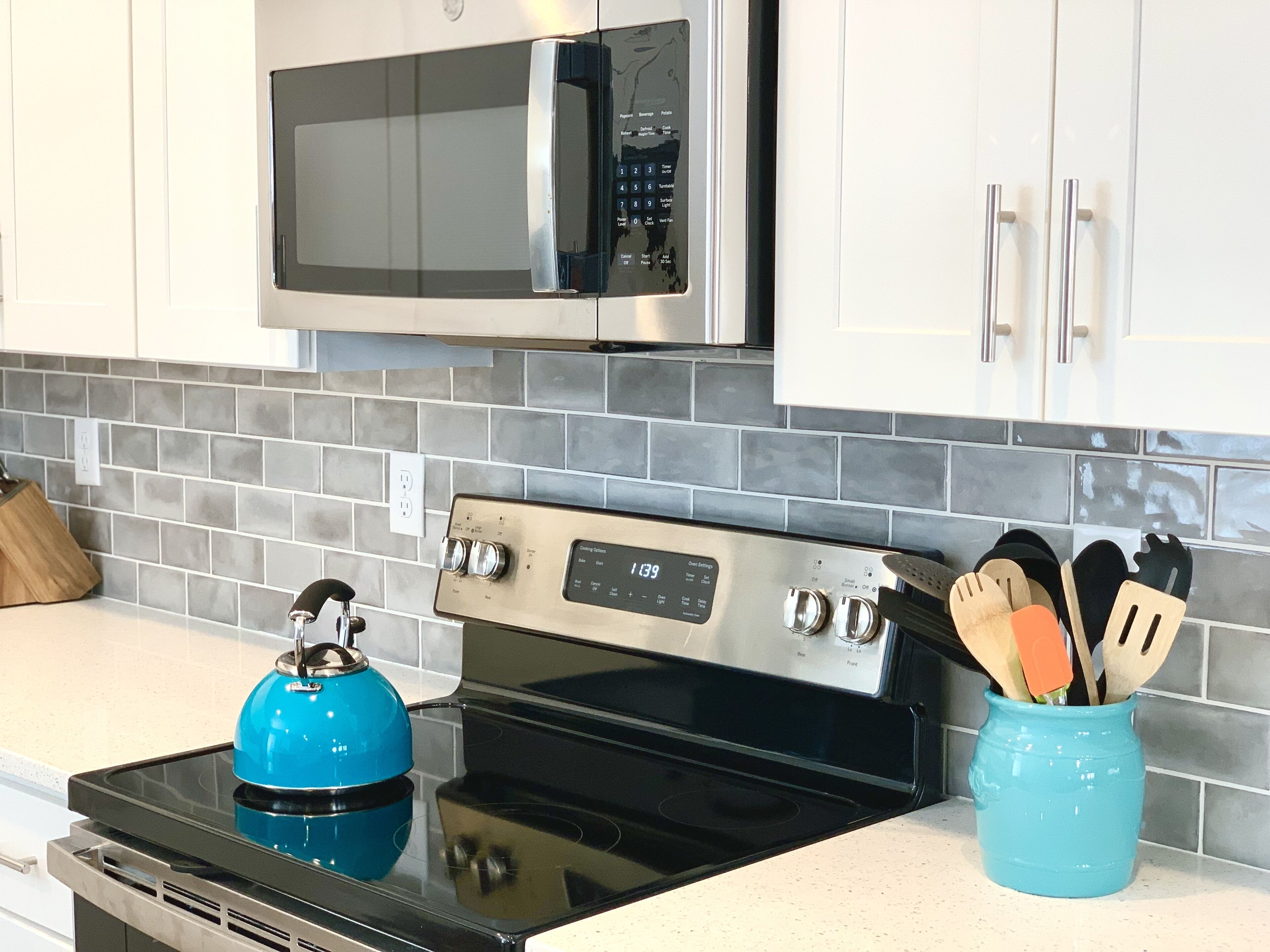 A kitchen with a black stove, a blue kettle, a microwave, and a utensil holder.