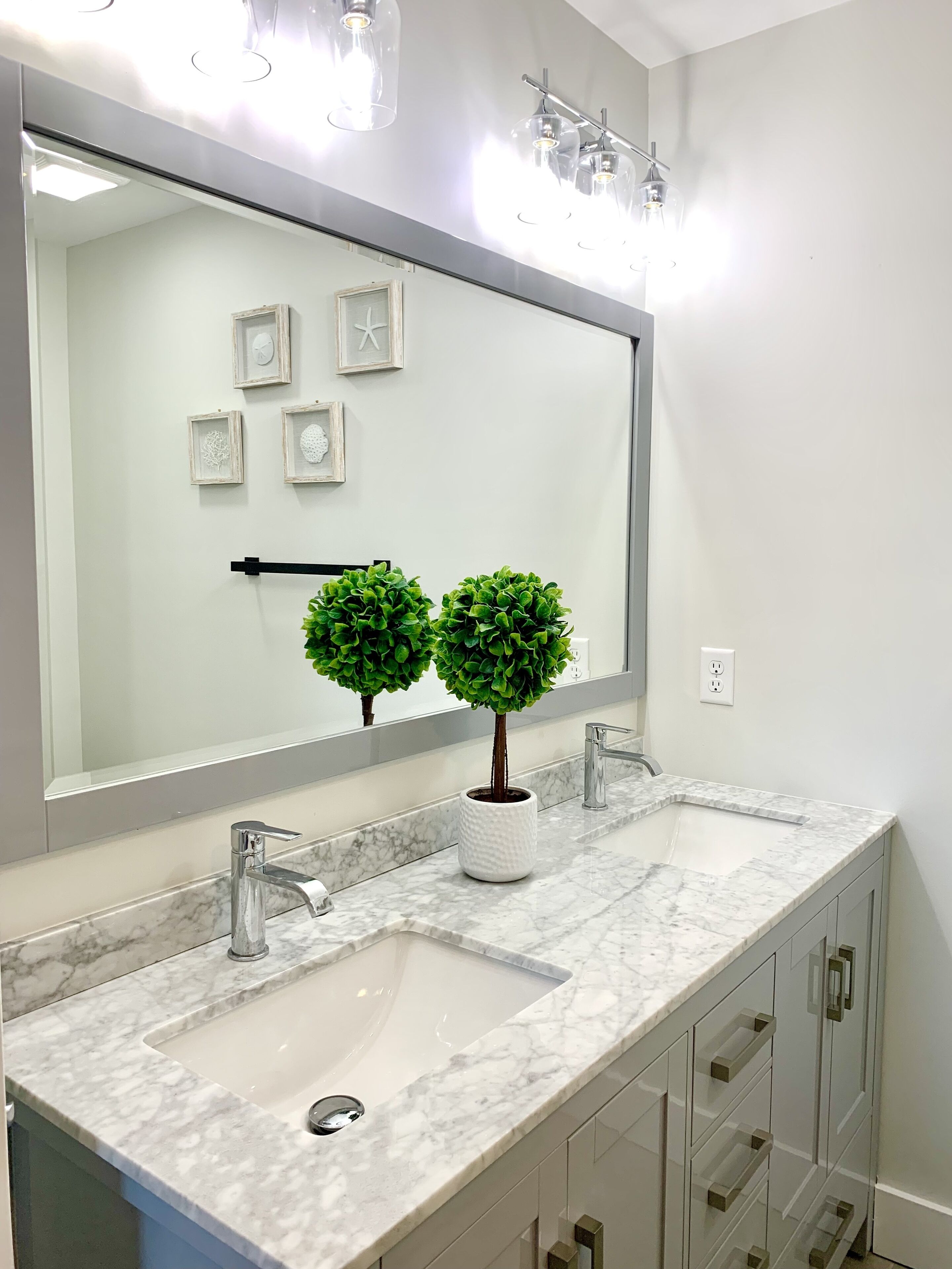 A bathroom with a large mirror, two sinks, a potted plant, and a modern faucet.