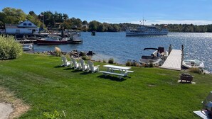 Une vue sur le lac, avec des bateaux amarrés, un espace pique-nique et une maison en arrière-plan.