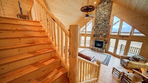 A wooden staircase leading to a living area with a stone fireplace, large windows, and a cozy seating area. - A True Montana Cabin with Sweeping Views of the Mountains and the Madison River. (Cameron)