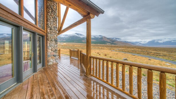 A wooden deck with stone pillars, large windows, and a view of mountains. - A True Montana Cabin with Sweeping Views of the Mountains and the Madison River. (Cameron)