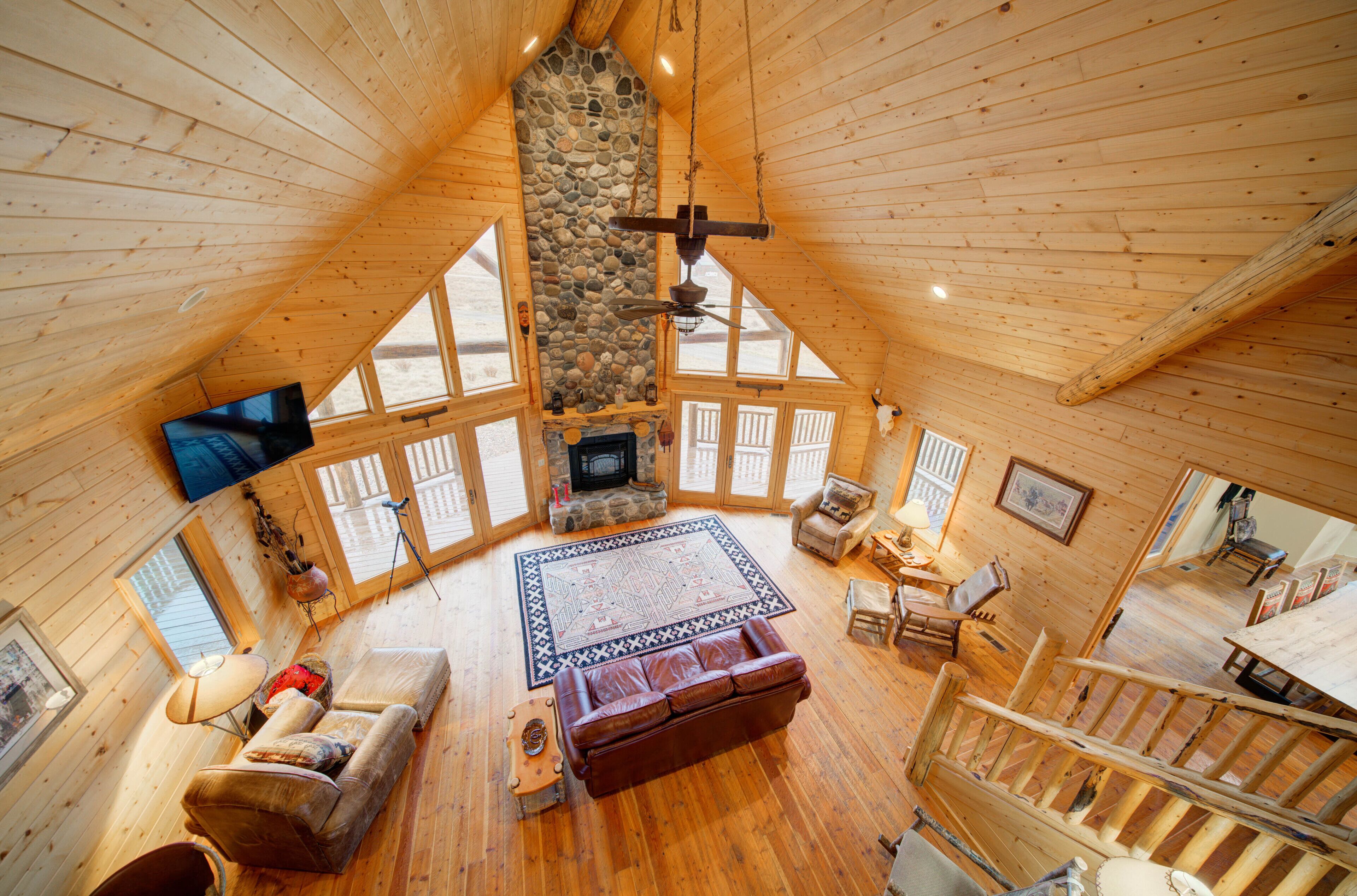 A spacious loft-style room with a stone fireplace, wooden floors, and large windows.